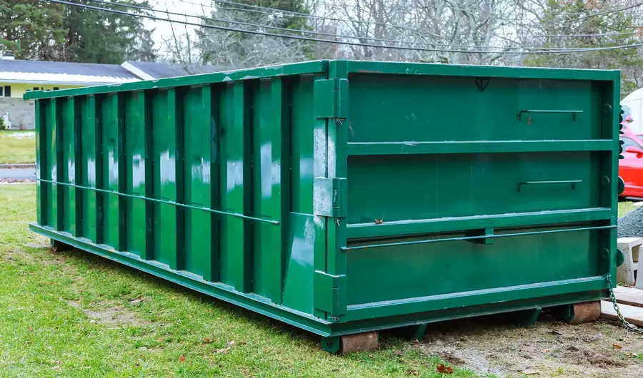 Green roll-off dumpster set on wooden boards on a residential lot